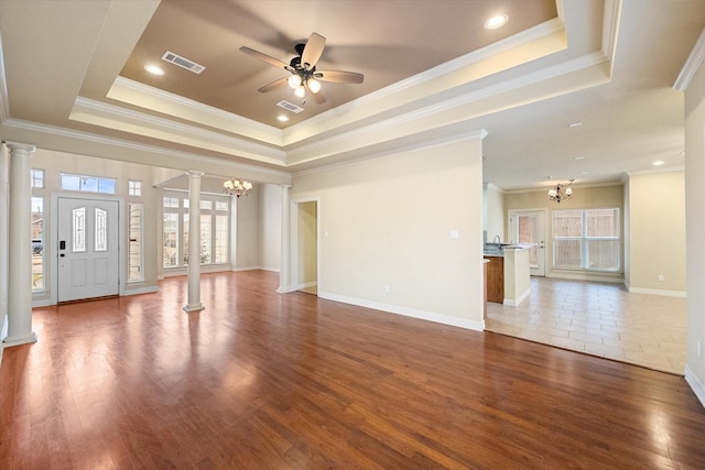 unfurnished living room featuring decorative columns, hardwood / wood-style flooring, ceiling fan with notable chandelier, and a tray ceiling