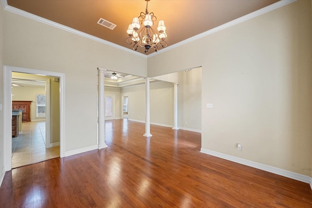 spare room with ornamental molding, ceiling fan with notable chandelier, wood finished floors, decorative columns, and a brick fireplace