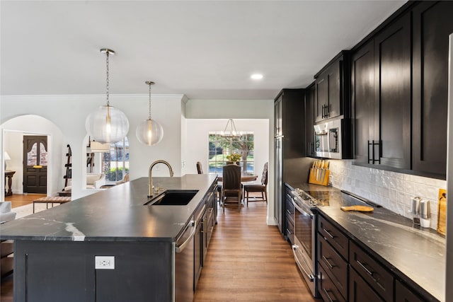 kitchen with pendant lighting, sink, backsplash, stainless steel appliances, and a center island with sink