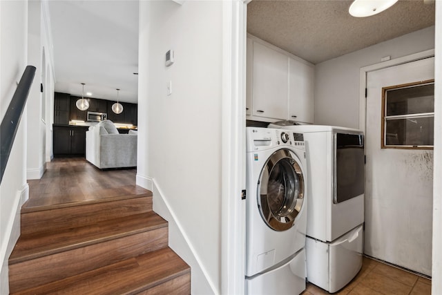 washroom with a textured ceiling, dark tile patterned floors, cabinets, and washing machine and clothes dryer