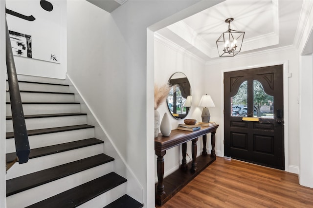 entrance foyer with a notable chandelier, a tray ceiling, wood-type flooring, and ornamental molding