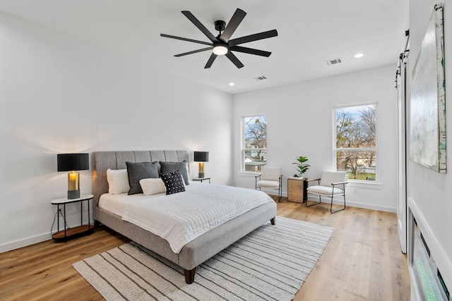 bedroom with ceiling fan, a barn door, and light wood-type flooring