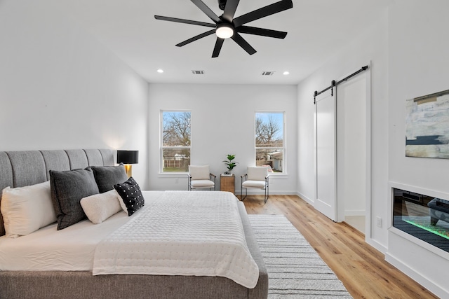 bedroom featuring ceiling fan, a barn door, and light hardwood / wood-style floors