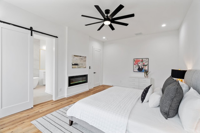 bedroom with ensuite bathroom, a barn door, hardwood / wood-style floors, and ceiling fan