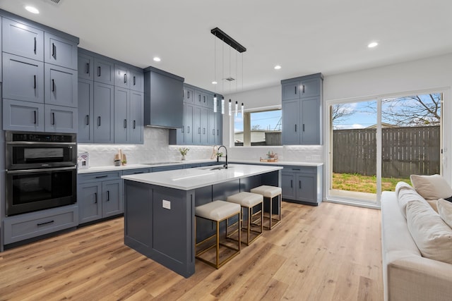 kitchen featuring hanging light fixtures, double oven, a kitchen breakfast bar, a center island with sink, and black electric cooktop