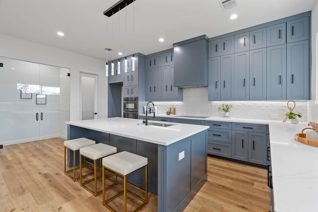 kitchen with a breakfast bar, sink, decorative light fixtures, light wood-type flooring, and an island with sink