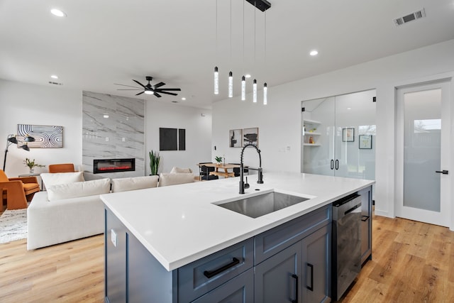 kitchen featuring sink, hanging light fixtures, stainless steel dishwasher, an island with sink, and a high end fireplace