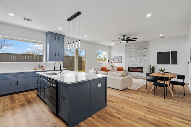 kitchen with sink, a center island with sink, dishwasher, pendant lighting, and a high end fireplace