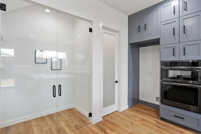 kitchen with gray cabinetry, double oven, and light hardwood / wood-style flooring