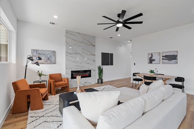 living room with ceiling fan, a high end fireplace, and light hardwood / wood-style flooring