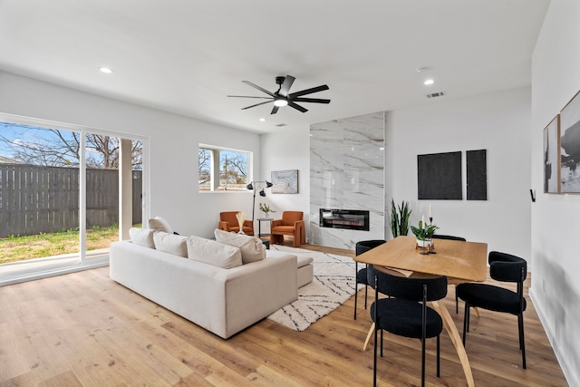 living room with ceiling fan, a fireplace, and light wood-type flooring