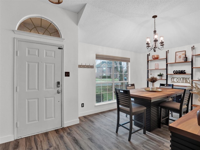 dining space with lofted ceiling, wood-type flooring, a chandelier, and a textured ceiling