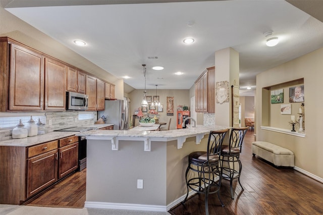 kitchen featuring a breakfast bar, appliances with stainless steel finishes, kitchen peninsula, pendant lighting, and decorative backsplash