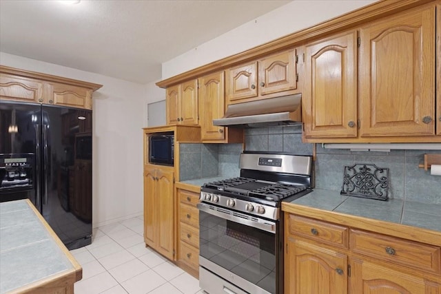 kitchen with light tile patterned floors, tile countertops, under cabinet range hood, black appliances, and backsplash