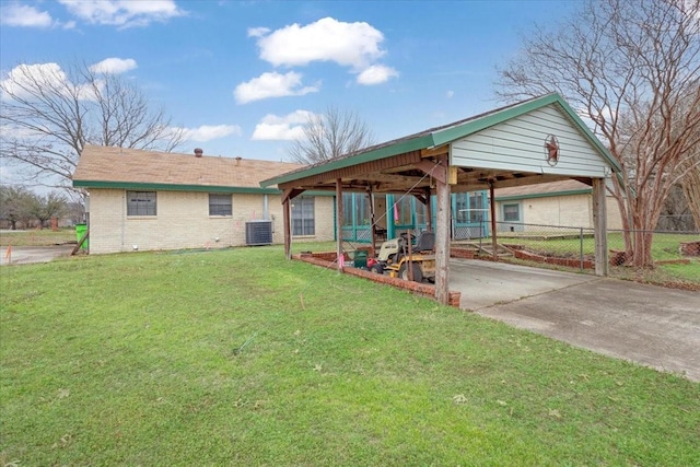 rear view of property featuring central air condition unit, brick siding, fence, a yard, and concrete driveway