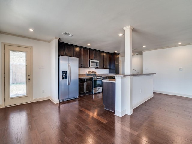 kitchen with dark wood-type flooring, appliances with stainless steel finishes, ornamental molding, light stone countertops, and an island with sink