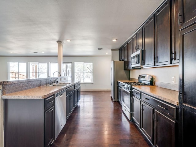 kitchen featuring sink, a kitchen island with sink, stainless steel appliances, dark brown cabinetry, and dark hardwood / wood-style flooring