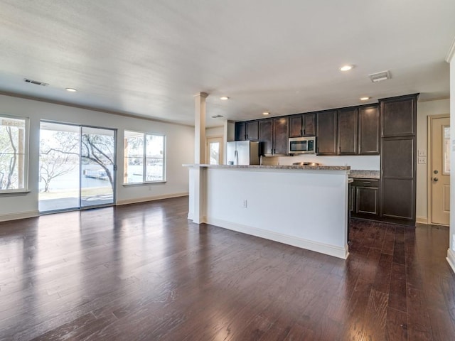 kitchen with a kitchen island, decorative columns, dark hardwood / wood-style flooring, dark brown cabinetry, and stainless steel appliances