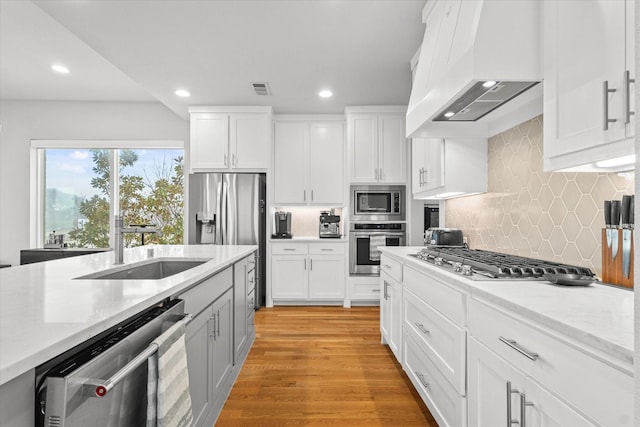 kitchen with sink, white cabinets, custom exhaust hood, light hardwood / wood-style floors, and stainless steel appliances