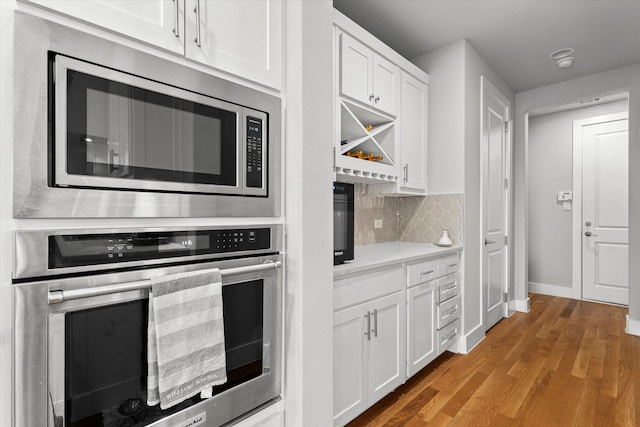 kitchen with stainless steel appliances, white cabinetry, backsplash, and light wood-type flooring