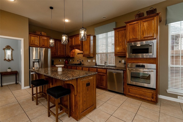 kitchen with decorative backsplash, appliances with stainless steel finishes, a kitchen island, and dark stone countertops