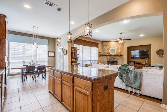 9720 Birdville Way, Fort Worth, TX 76244 - kitchen with a fireplace, dark stone countertops, a ceiling fan, a kitchen island, and brown cabinets