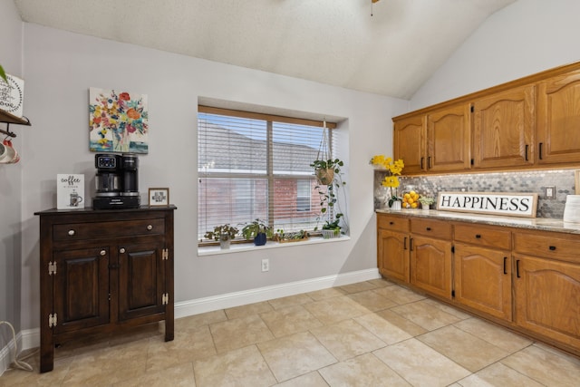 kitchen featuring lofted ceiling, backsplash, light tile patterned floors, and light stone countertops