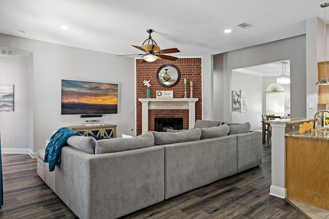 living room featuring ceiling fan, ornamental molding, dark hardwood / wood-style floors, and a fireplace