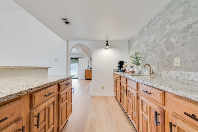 2410 Cedar Elm Ln, Garland, TX 75043 - kitchen with a sink, light wood-style floors, arched walkways, light stone countertops, and an accent wall
