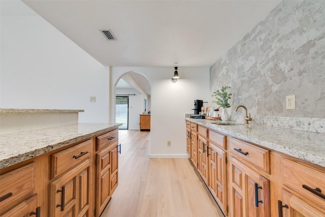 kitchen with light stone counters, sink, and light wood-type flooring