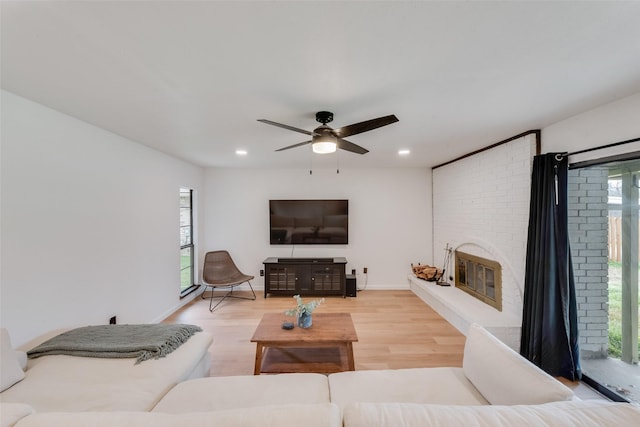 living room with hardwood / wood-style flooring, ceiling fan, and a brick fireplace