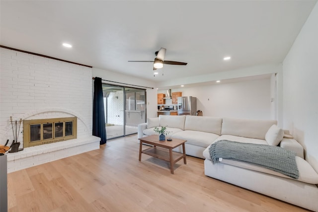 living room with ceiling fan, a brick fireplace, and light wood-type flooring