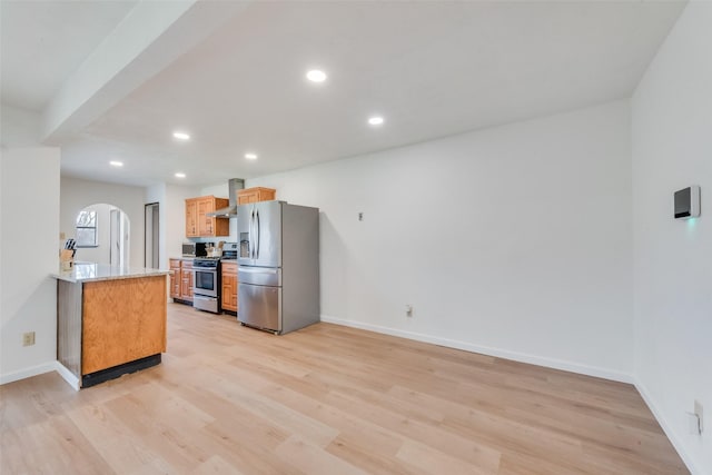 kitchen featuring wall chimney range hood, light wood-type flooring, light stone countertops, and appliances with stainless steel finishes