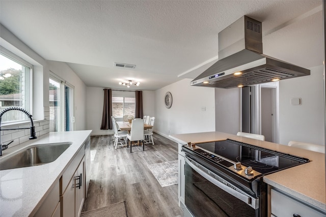 kitchen featuring sink, island range hood, a textured ceiling, stainless steel appliances, and light hardwood / wood-style floors