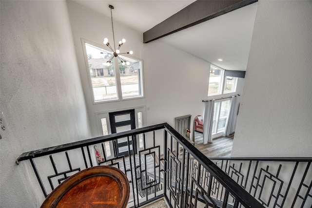 staircase with beam ceiling, a chandelier, hardwood / wood-style floors, and a high ceiling