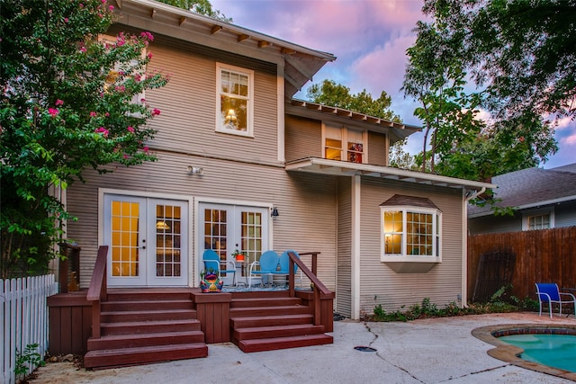 back house at dusk featuring a fenced in pool, a patio area, and french doors