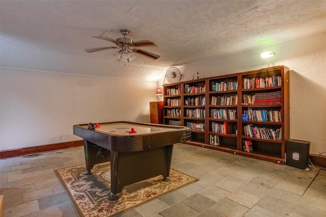 recreation room with ceiling fan and a textured ceiling