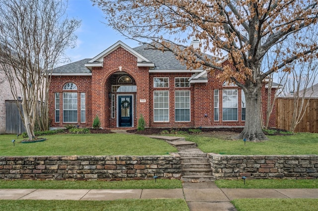 traditional-style home with a front lawn, fence, brick siding, and a shingled roof