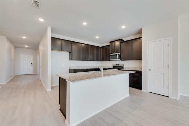 kitchen with sink, a kitchen island with sink, stainless steel appliances, light stone countertops, and light hardwood / wood-style flooring