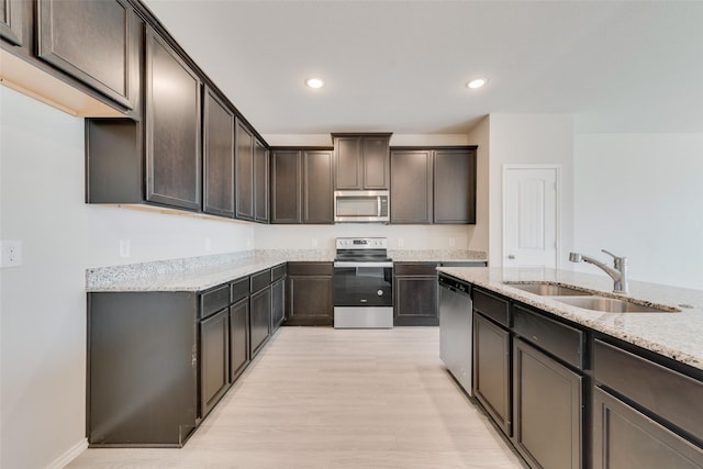 kitchen featuring dark brown cabinetry, appliances with stainless steel finishes, light stone countertops, and sink