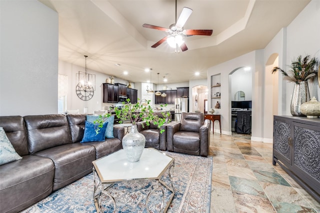 15805 Rockingham St, Frisco, TX 75036 - living room featuring ceiling fan, a raised ceiling, arched walkways, a chandelier, and light stone finish flooring