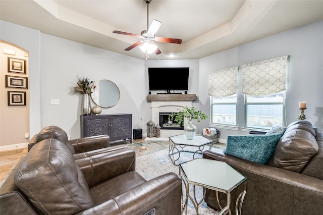 15805 Rockingham St, Frisco, TX 75036 - living area with arched walkways, a ceiling fan, a raised ceiling, baseboards, and a glass covered fireplace