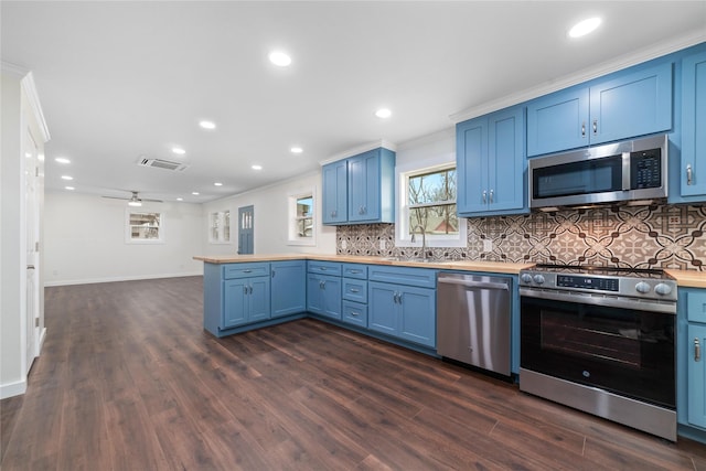 kitchen featuring visible vents, a peninsula, blue cabinetry, a sink, and appliances with stainless steel finishes