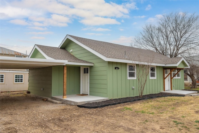 back of property with an attached carport, board and batten siding, and roof with shingles