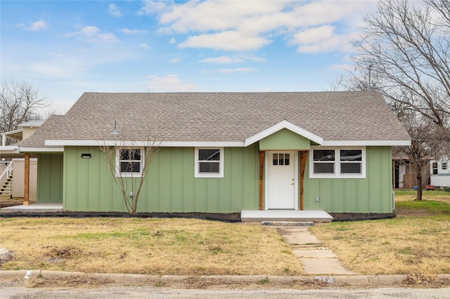 view of front of home featuring board and batten siding, roof with shingles, and a front yard