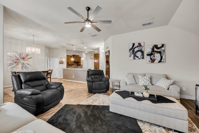 living room featuring ceiling fan with notable chandelier, vaulted ceiling, and light hardwood / wood-style floors