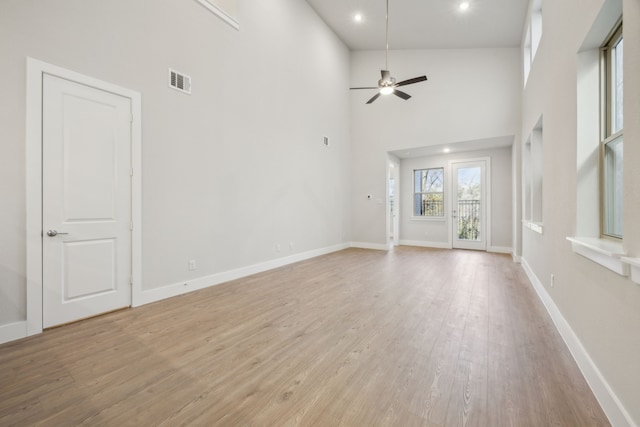 unfurnished living room featuring a high ceiling, ceiling fan, and light hardwood / wood-style floors