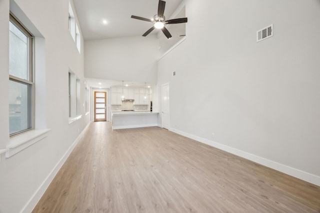 unfurnished living room with a high ceiling, ceiling fan, and light hardwood / wood-style flooring