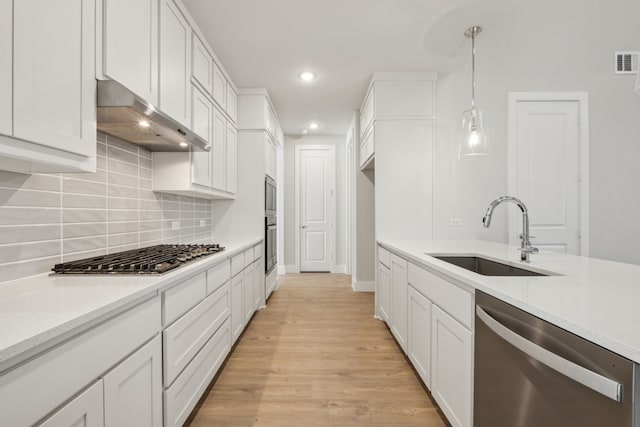 kitchen featuring appliances with stainless steel finishes, pendant lighting, white cabinetry, sink, and light hardwood / wood-style flooring