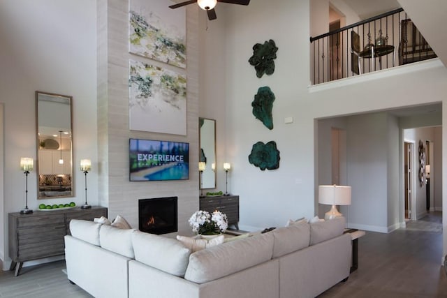 living room with a high ceiling, hardwood / wood-style flooring, a large fireplace, and ceiling fan